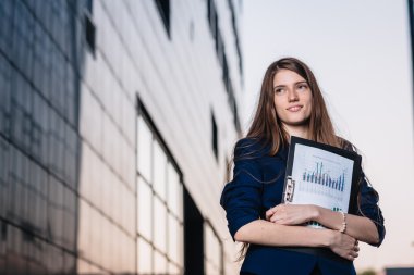 Successful smiling businessman, standing against the backdrop of buildings holding  folder with sales charts. City business woman working.