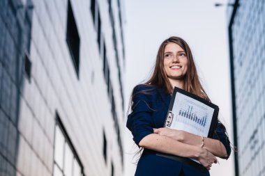 Successful smiling businessman, standing against the backdrop of buildings holding  folder with sales charts. City business woman working.