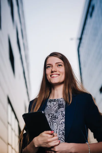 Empresário bem sucedido sorrindo, de pé no fundo dos edifícios e segurando um computador tablet. Cidade mulher de negócios trabalhando . — Fotografia de Stock