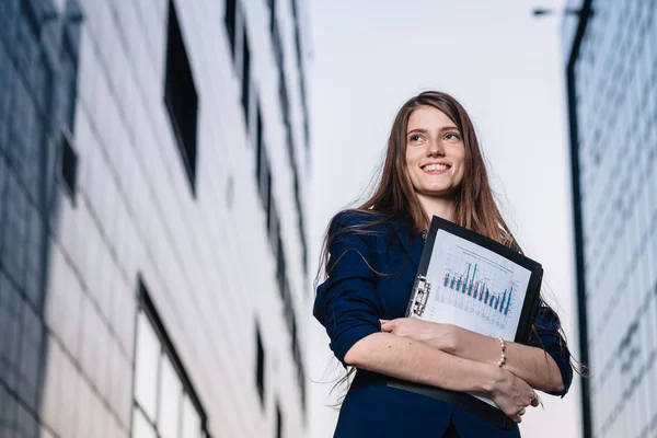 Successful smiling businessman, standing against the backdrop of buildings holding  folder with sales charts. City business woman working. — Stockfoto