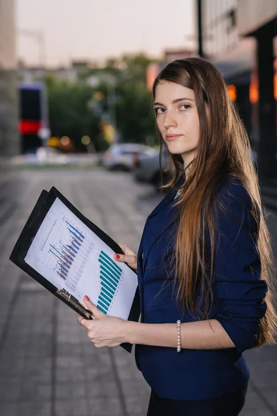 Successful smiling businessman, standing against the backdrop of buildings holding  folder with sales charts. City business woman working. — Stok fotoğraf