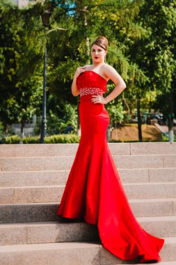 Uzun kırmızı Abiye ayakta ağaçlar ve çalılar arka plan üzerinde güzel kız