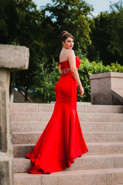 Uzun kırmızı Abiye ayakta ağaçlar ve çalılar arka plan üzerinde güzel kız