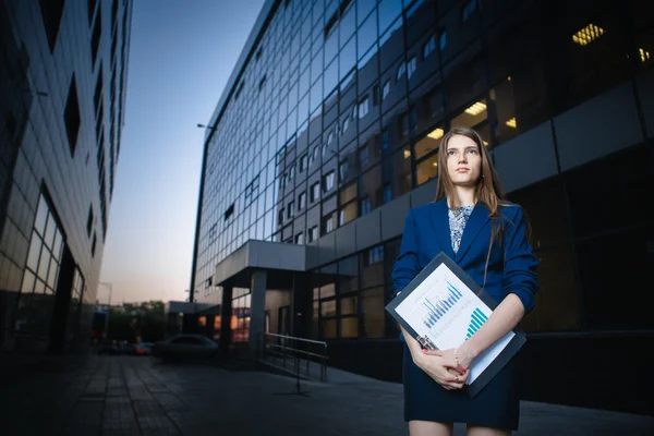 Mulher de negócios bonita bem sucedida de pé contra um fundo de edifícios e pasta de retenção . — Fotografia de Stock