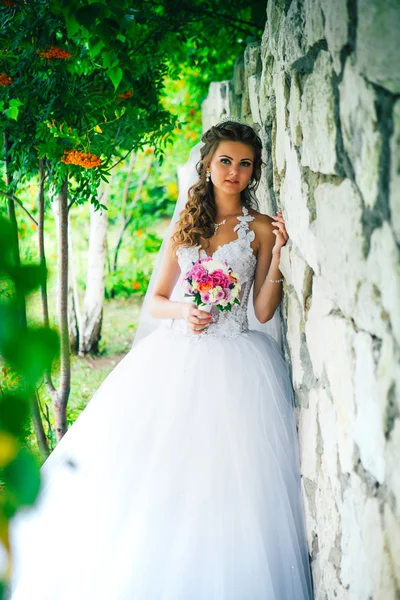 Hermosa joven novia de pie sobre un fondo de pared de piedra — Foto de Stock