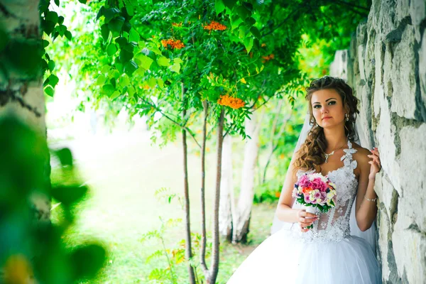 Mooie jonge bruid permanent op een stenen muur achtergrond — Stockfoto