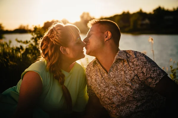 Romantiska par sit och kyssas på bakgrunden sommaren sjö — Stockfoto