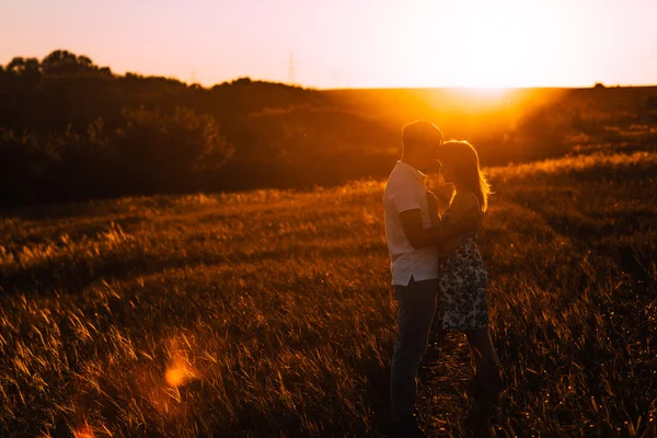 Romantikus pár állt, és a háttérben nyári rét sunset csók — Stock Fotó