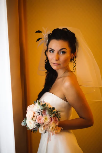 Krásná mladá šťastná nevěsta stojící u okna — Stock fotografie