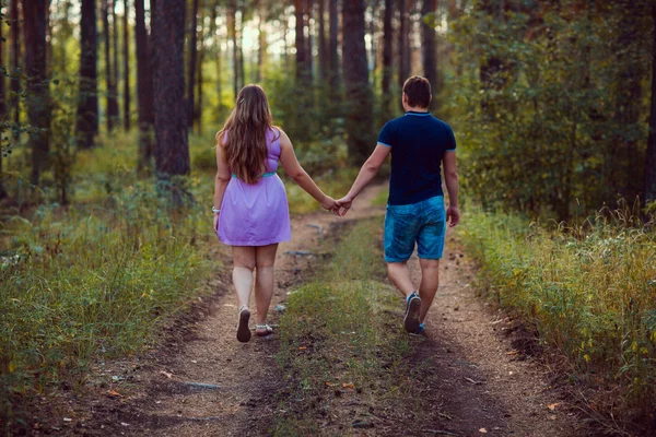 Romántica pareja joven ir y tomarse de la mano en el bosque de verano de fondo — Foto de Stock