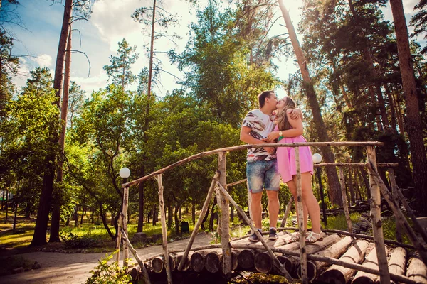 Romántica pareja joven besándose y de pie para puente en el bosque de verano de fondo — Foto de Stock