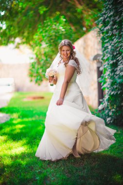 Şık güzel mutlu gelin buket çiçek bir arka plan üzerinde yaz park tam uzunlukta ağaçlarda tutarak.