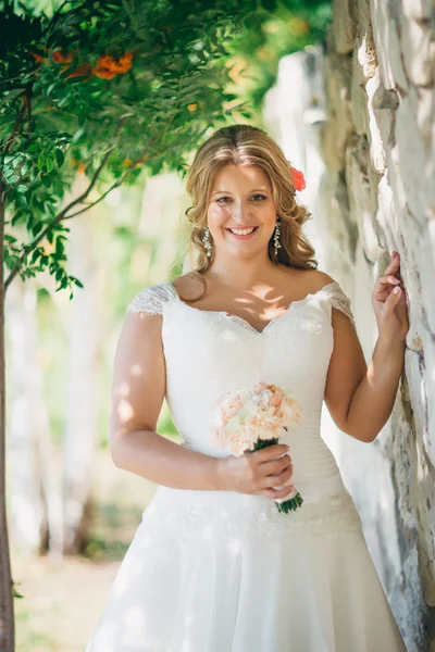 Стильная красивая счастливая невеста с букетом цветов на фоне каменной стены — стоковое фото