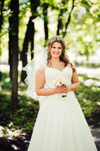 Elegante bella sposa felice tenendo bouquet di fiori su uno sfondo alberi nel parco estivo primo piano — Foto Stock