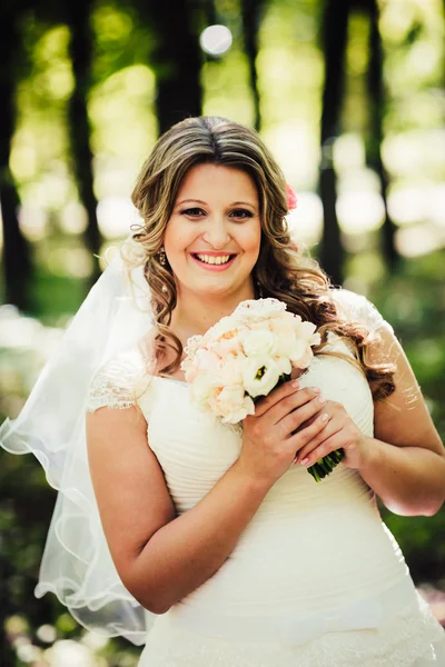 Stylish beautiful happy bride holding  bouquet of flowers on a background trees in the summer park close-up — Stock Photo, Image