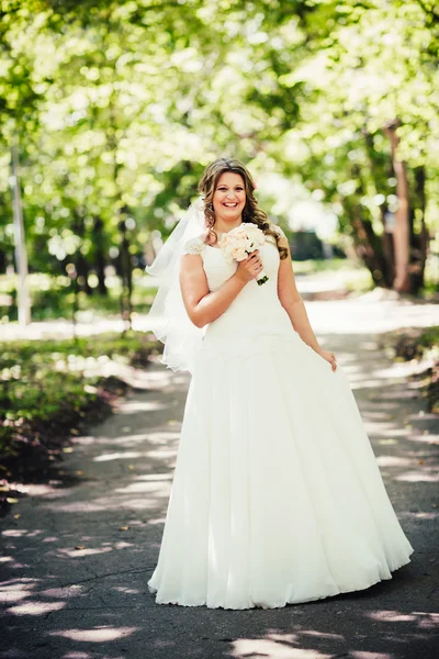 Noiva feliz bonita elegante que mantém o buquê de flores em umas árvores de fundo no parque de verão comprimento cheio — Fotografia de Stock