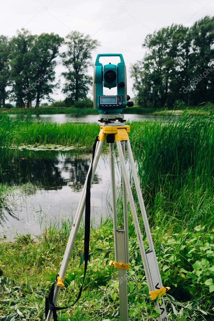 blue surveying equipment total station on a background of lake and forest