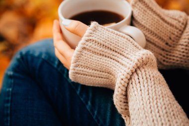 Genç kadın bir kazak ve jeans sonbahar arka plan üzerinde çay içmek rahatlatıcı