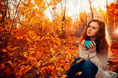 Genç kadın bir kazak ve jeans sonbahar arka plan üzerinde çay içmek rahatlatıcı