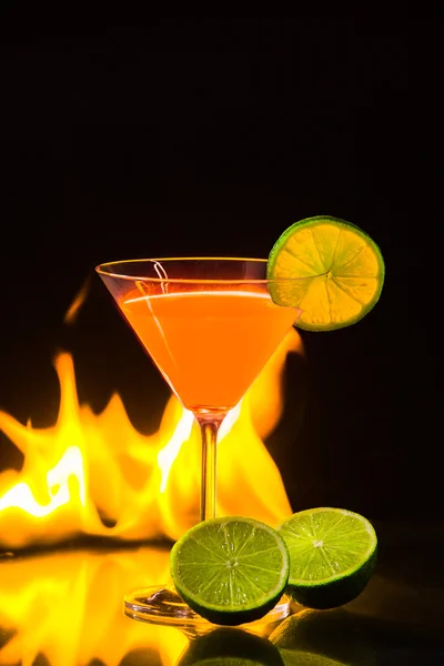 Colorful orange cocktail in nice carroty color to front of a black background and fire — Stock Photo, Image