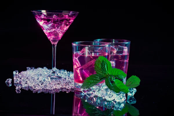 Copo de vinho e dois copos com martinis rosa, fragmentos finos de gelo, hortelã fresca em um fundo de espelho escuro — Fotografia de Stock