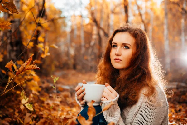 Young woman in a sweater and jeans relaxing drink tea on autumn background — Stock Photo, Image