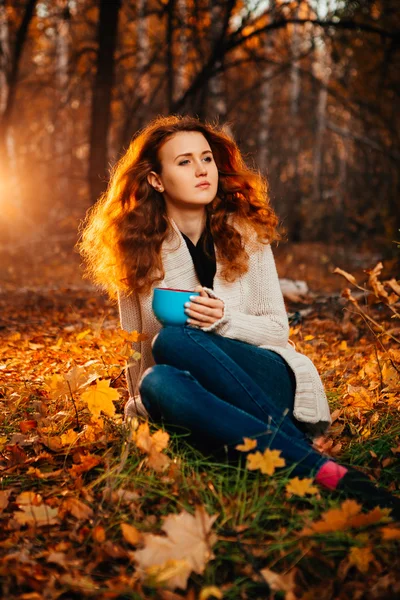 Junge Frau in Pullover und Jeans trinkt entspannt Tee auf herbstlichem Hintergrund — Stockfoto