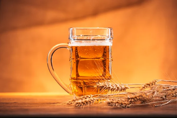 Кружка светлого пива с колосьями пшеницы на деревянном столе — стоковое фото