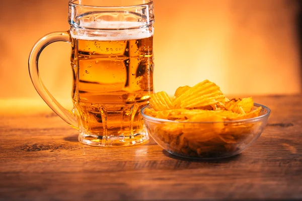 Светлая кружка пива с миской картофельных чипсов на деревянном столе — стоковое фото