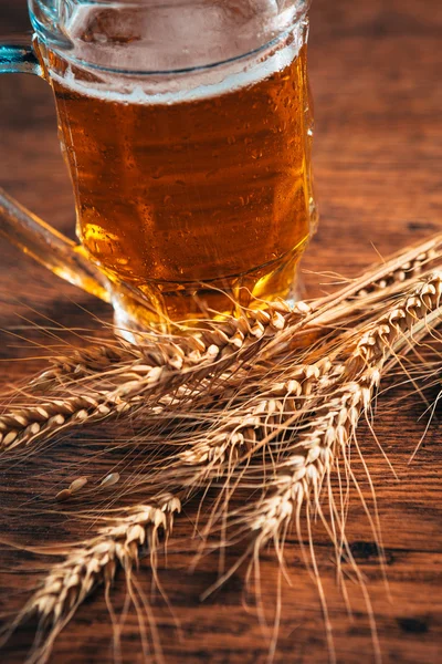 close-up mug of light beer with ears of wheat on the wooden table