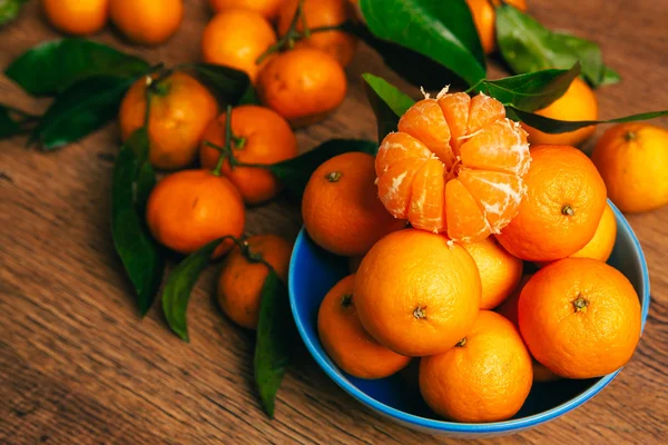 Viele frische Mandarinen in einer blauen Schüssel, die auf einem Holztisch steht — Stockfoto