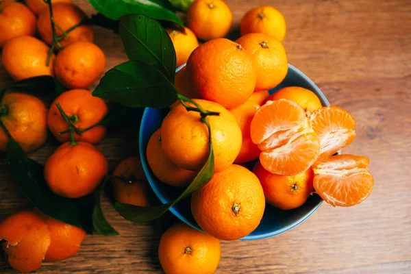 Muchas naranjas frescas de mandarina en un tazón azul, de pie sobre una mesa de madera —  Fotos de Stock