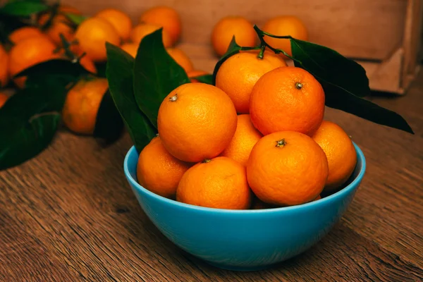 Viele frische Mandarinen in einer blauen Schüssel, die auf einem Holztisch steht — Stockfoto