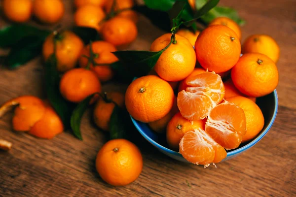 Muchas naranjas frescas de mandarina en un tazón azul, de pie sobre una mesa de madera —  Fotos de Stock