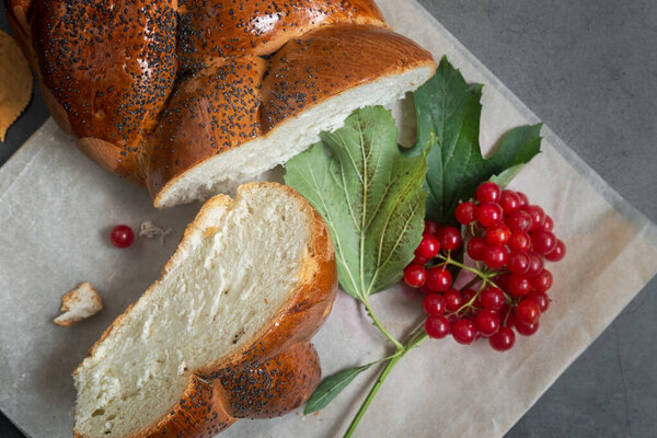 On the table is a sliced loaf of white bread with a crisp crust sprinkled with poppy seeds. Next to the knife and viburnum berries. Front view, dark background, copy space