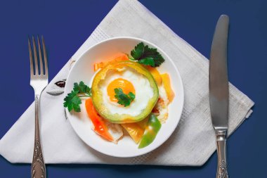 Tabağın üzerindeki masada biberin içinde yumurta olan fırında pişmiş dolmalık biber var. Yakınlarda bir peçetede çatal bıçak takımı var. Kopyalamak için en üstteki görünüm. Düz yatıyordu