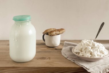 Ahşap masada bir cam süt kavanozu, bir tabak ev yapımı süzme peynir ve turta var. Ön görünüm, boşluğu kopyala.