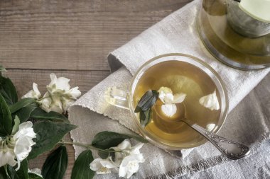 Masanın üzerinde, peçetenin üzerinde yasemin çiçeklerinin yanında yasemin çayı ile bir fincan ve çaydanlık var. Üst görünüm, alanı kopyala