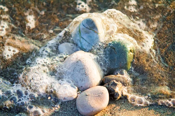 Pequenas pedras marinhas no litoral, cobertas por uma onda marítima . — Fotografia de Stock