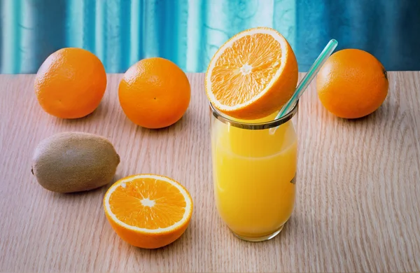 Suco de laranja em um copo e laranjas na mesa . — Fotografia de Stock