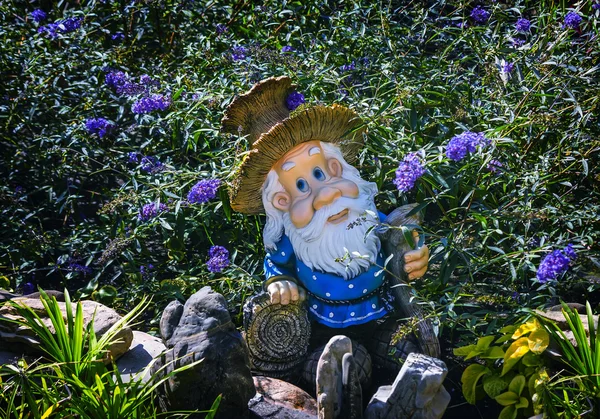 Interesting statue of a dwarf among the flowers. — Stock Photo, Image