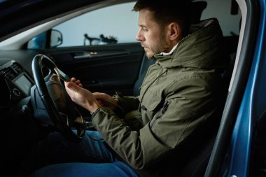 Şoför koltuğunda oturan ve içerideki akıllı telefona bakan bir adam. Mobil teknoloji kavramı, navigasyon