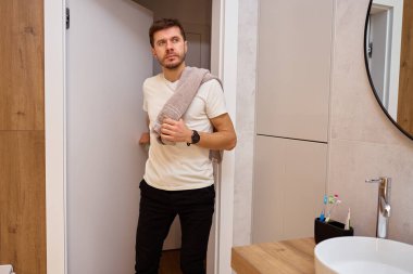 Modern banyoda duran bir adam havluyu omuzunda tutuyor ve hijyen rutininden sonra kapıyı açıyor. Sabah rutini kavramı