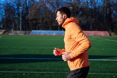 Turuncu spor ceketli bir adam stadyumda koşuyor. Dayanıklılık eğitimi kavramı