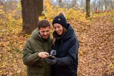 Kadın ve erkek, sonbahar parkındaki akıllı telefon ekranına bakarak birbirlerine yakın duruyorlar. Çift ilişkisi kavramı