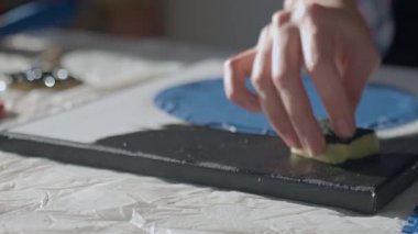 Örtülü çalışma masasında sünger kullanarak tuval yüzeyine siyah boya sürerken elinizi kapatın. Dokulu sanat yaratımı ve yaratıcı süreç kavramı