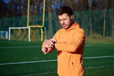 Spor ceketli bir adam açık hava spor sahasında dikilirken akıllı bakışlara bakıyor. Fitness izleme kavramı