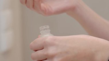 Kadın ellerinin evdeki banyoda küçük bir cilt bakımı şişesini açması. Cilt ürünü kullanımı kavramı