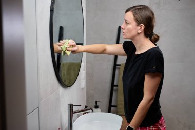 Lavaboda dururken banyo aynasını temizleyen kadın. Ev temizliği kavramı