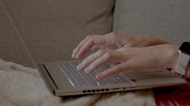 Eller evdeki koltukta otururken dizüstü bilgisayarda klavyede yazıyor. Uzak çalışma kavramı